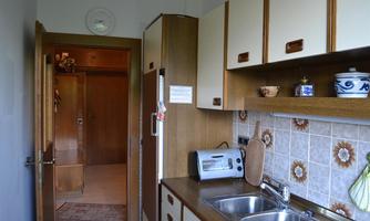 A small kitchen with wooden cabinets and a double sink. In the background, an open door to another room is visible.