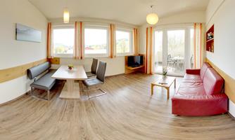 A bright living room with large windows and modern furniture. The space is cozy with a red sofa and a dining area.