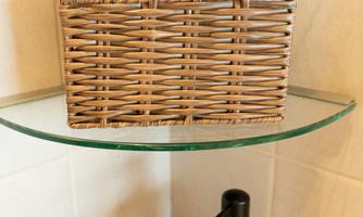 An elegant bathroom area with a wicker basket containing two towels. Below it is a small wooden container with soap and a dish with hygiene items.