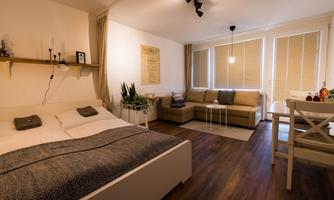 A modern room with a double bed and a cozy seating area. Large windows provide plenty of daylight.