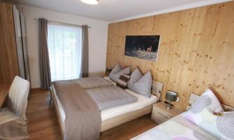 A cozy bedroom with two beds and wood paneling. The bright colors and large windows create an inviting atmosphere.