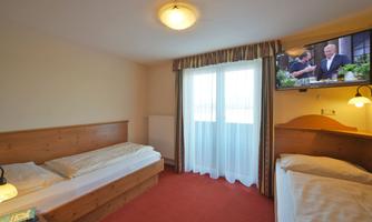 A simple room with two beds and a television on the wall. The room has a window with curtains and a carpeted floor.