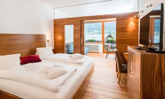 A cozy hotel room with a double bed and wooden furniture. The large window front offers a view of nature.