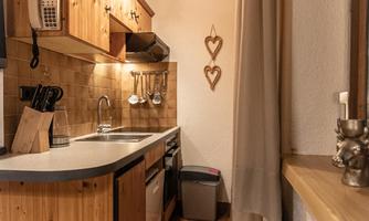 A cozy kitchen with wooden furniture and warm lighting. The walls are paneled with wood, and there are decorative hearts as accents.