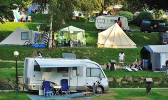 A campsite with several tents and a motorhome. The surroundings are green and are well suited for relaxing outdoors.
