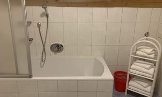 A simple bathroom with a bathtub and a shower. Towels are neatly stacked on a white shelf.
