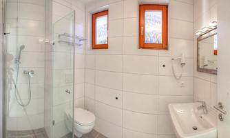 A modern bathroom with a shower and sink. It features bright tiles and orange window frames.
