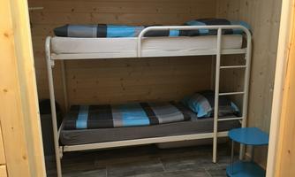 A simple room with a bunk bed and a small table. The walls are made of wood, and the bedding has a modern pattern in blue and gray.