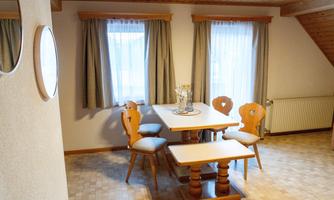 A cozy dining area with a table and chairs. The large windows allow plenty of daylight to come in.