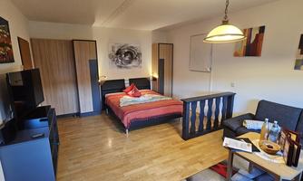 A cozy room with a double bed and a seating area. The furniture is modern and there are artworks on the walls.