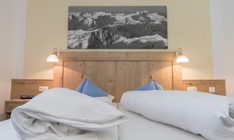 A modern bedroom with a wooden bed and two blue pillows. A large black-and-white picture of mountains hangs on the wall.