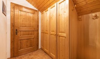 A bright hallway with a wooden door and a wooden cabinet. The ceiling is also paneled with wood.