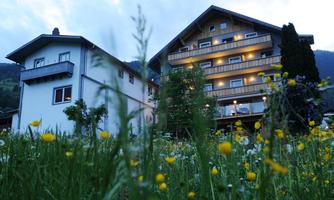 A beautiful building in nature, surrounded by colorful flowers and a clear sky. The facade is illuminated and creates a cozy atmosphere.