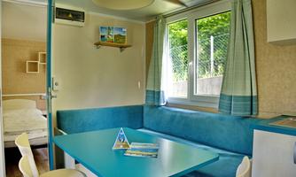 A cozy, modern living space with a blue table and white chairs. Light pours in through the windows, offering a view of the greenery.