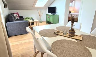 A bright and modern apartment with a living area and a dining table. Pleasant wooden floors and simple furniture create an inviting atmosphere.