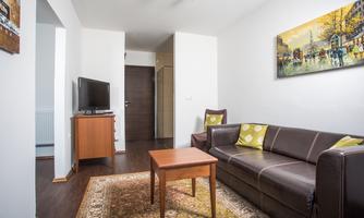 A bright living room with a brown sofa, a table, and a television. A colorful painting hangs on the wall.
