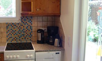 A modern kitchen with a stove, dishwasher, and a small coffee area. The walls are decorated with colorful tiles.