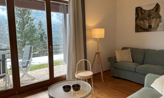 A cozy living room with a sofa and an unusual wolf painting on the wall. Large windows offer a view of a winter landscape outside.