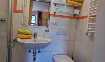 A modern bathroom with a shower, sink, and toilet. Towels in yellow and green complement the comfortable design.