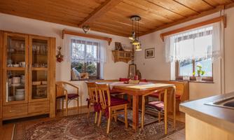 A cozy dining area with a wooden table and chairs. The room has wooden ceilings and large windows with plenty of natural light.