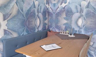 A cozy dining area with a wooden tray and a cushioned bench. The wall is decorated with a blue flower design.