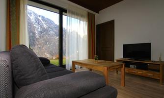 A modern living room with a gray sofa and a wooden table. Large windows provide a view of the mountains.