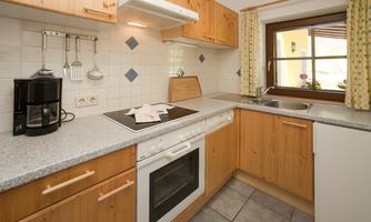 A modern kitchen with wooden cabinets and a gray work area. It features a stove, a sink, and a window with a view outside.