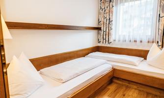A simple bedroom with two beds and wooden details. The room has a window with curtains and a light, friendly look.