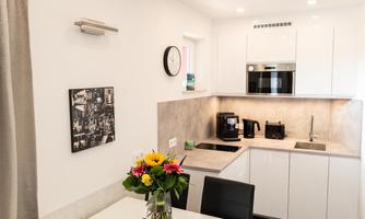 A modern kitchen with a white table and black chairs. A flower vase is on the table, and the kitchen furnishings are bright and functional.
