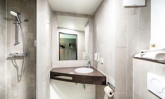 A modern bathroom with a shower and a sink. The walls are tiled in light colors, and there is a large mirror.
