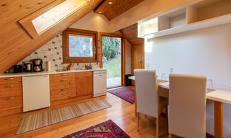 A modern kitchen with wooden paneling and large windows. The open space includes a table and chairs as well as a cozy atmosphere.