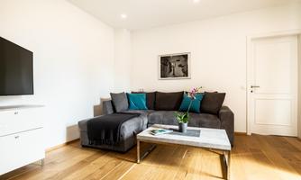 A modern living room with a gray sofa and cool blue cushions. The room features a television and a simple coffee table.