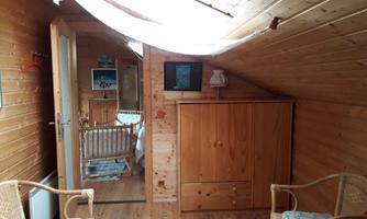 A cozy attic room with wood paneling. There is a crib, a wardrobe, and two wicker armchairs.