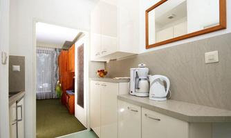 A modern kitchen with white cabinets and a kettle. In the background, a cozy living area is visible.
