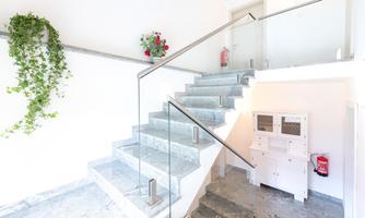 A modern staircase made of marble with a clear railing. A plant arrangement hangs on the wall and there is a mailbox on the ground floor.