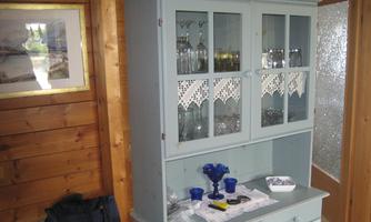 A blue cupboard buffet with glasses inside stands next to a wooden wall. On the table, some blue glasses and tools are visible.