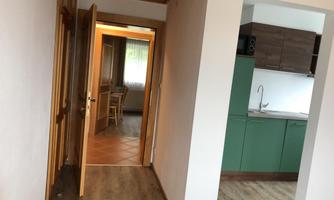 A bright hallway with an open door leading to another room. On the left side, there is a green kitchenette.