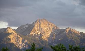 A majestic mountain under a cloudy sky. The sun rays give the mountain peak a golden shimmer.