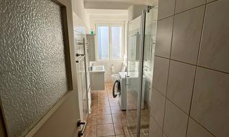 A bright hallway in the bathroom with tiled flooring and a large shower cubicle. A window provides natural light.