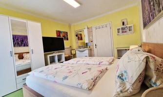 A cozy bedroom with yellow walls and a double bed. There is a large wardrobe, a television, and decorative pictures on the walls.