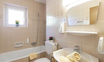 A modern bathroom with a bathtub, a sink, and a window. The walls are tiled in light colors and there are some decorative elements present.