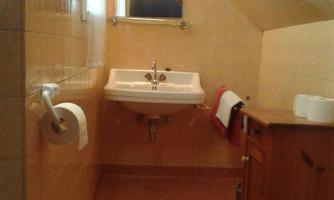 A small bathroom with sloping walls and a sink. There is also a wooden cabinet and a towel.
