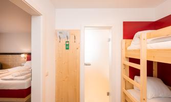 A bright room with a wooden bunk bed and a white room. In the background, there is a closed door and a simple, modern design visible.