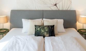 A modern bedroom with a large double bed and soft pillows.  
Next to the bed are two nightstands with lamps, and a decorative picture hangs on the wall.