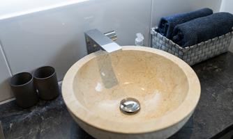 A modern sink made of bright natural stone stands on a dark surface. Next to it are two black cups and a basket with blue towels.