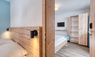 A modern room with wooden details and a separate living area. There is a bed, a television, and a wardrobe.