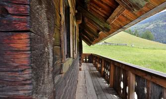 A rustic wooden house with a balcony and a view of a green meadow. The surroundings are quiet and natural.