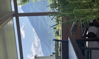 A cozy terrace with a view of mountains and a lake. The sky is clear with some clouds.