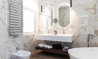 A modern bathroom with marbled walls and elegant mirrors. The amenities include a sink, a bathtub, and a towel holder.