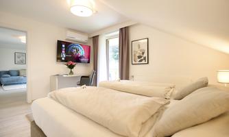 A modern bedroom with two beds and a television. The room is bright and friendly, with access to a balcony.